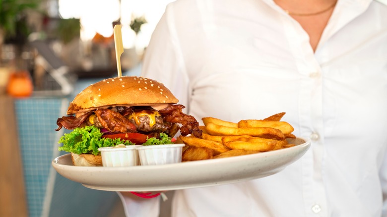 A waitress serving a bacon burger and fries