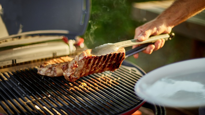 man turning over steak charcoal grill