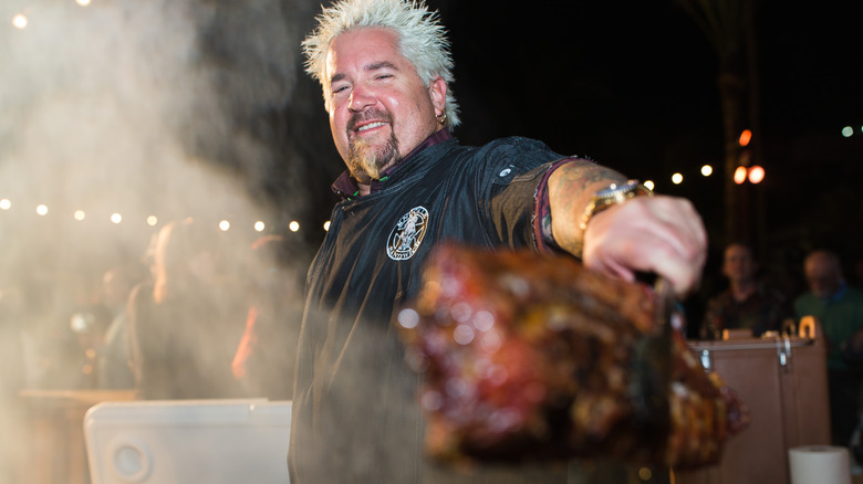 Guy Fieri holding barbecue with tongs