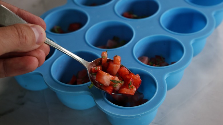 spooning strawberries into ice tray